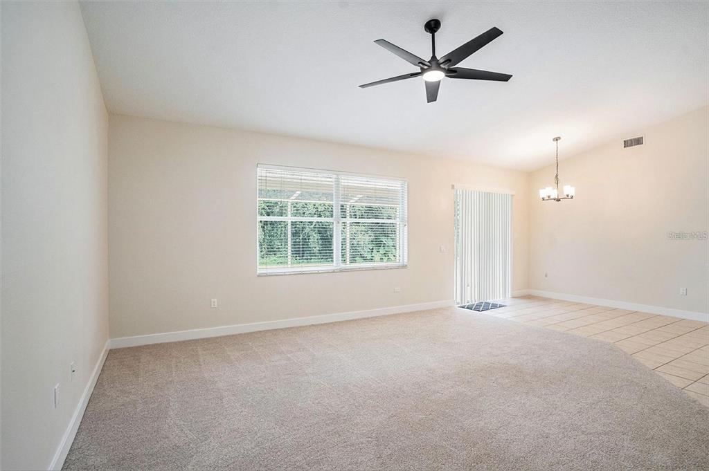 A carpeted living room features a ceiling fan, a large window, and a tiled dining area — 16909 FALCONRIDGE ROAD, LITHIA, FL
