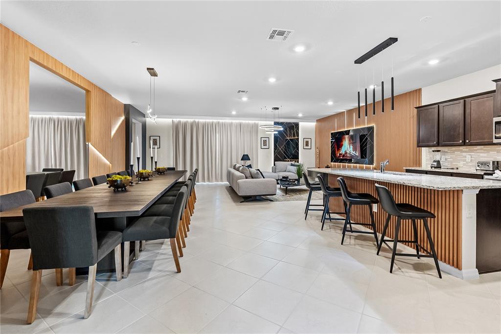 A spacious open-concept room features a long dining table, a kitchen island, and a living area — 15969 CAPE CORAL LOOP, CLERMONT, FL