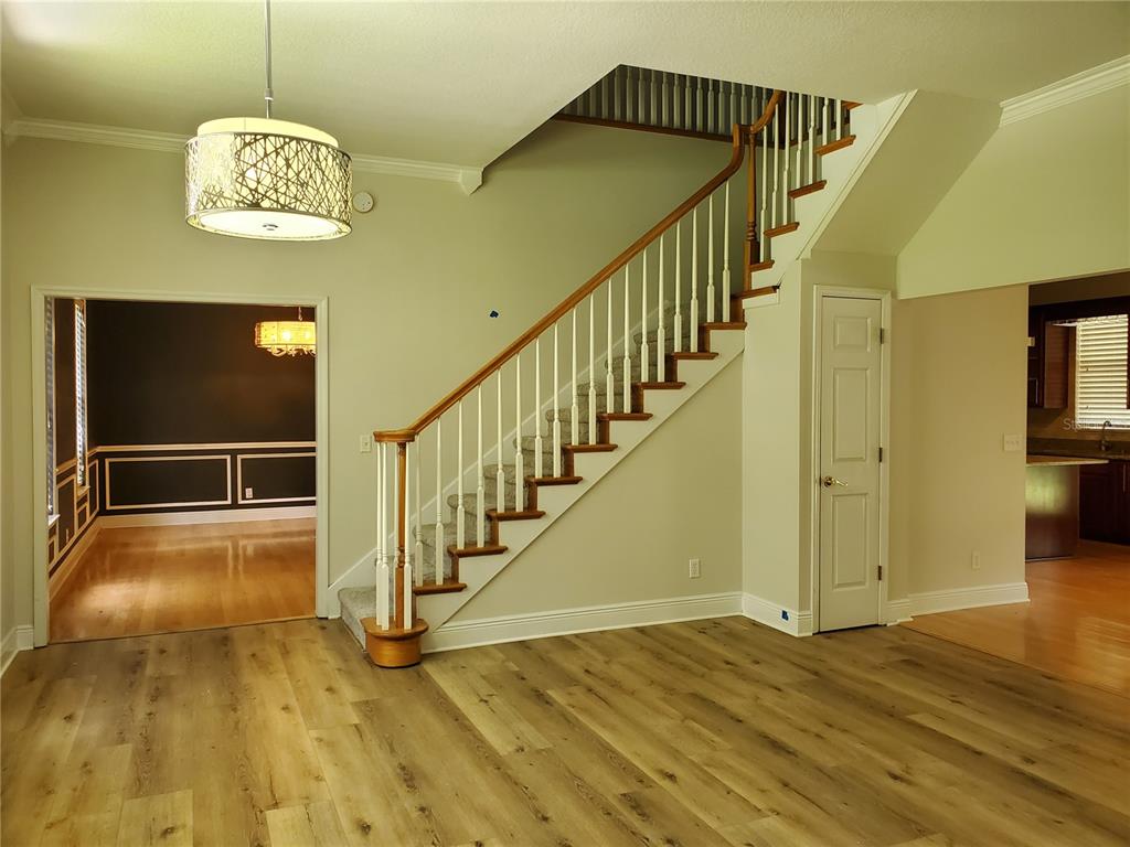 A living room with wood-look flooring, a staircase, and a view into a kitchen area — 2121 FAIRFIELD AVENUE, BRANDON, FL
