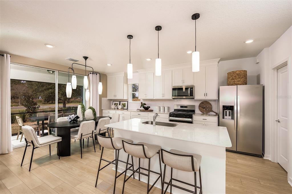 A modern kitchen features white cabinetry, a quartz island with bar seating, and an adjacent dining area — 16817 HARMONY RIVER LANE, PARRISH, FL