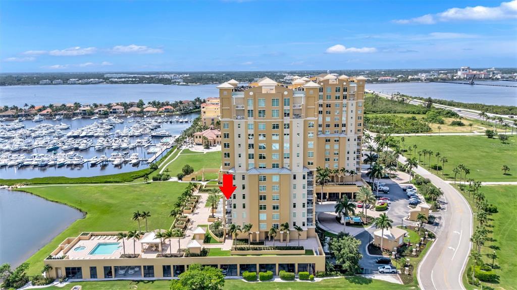 An aerial view shows a tall, tan residential building next to a marina and pool — 140 RIVIERA DUNES WAY UNIT 401, PALMETTO, FL