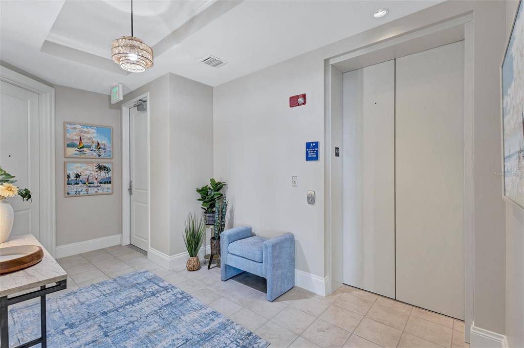 A hallway features a blue upholstered bench, a patterned rug, and a closed elevator door — 140 RIVIERA DUNES WAY UNIT 401, PALMETTO, FL