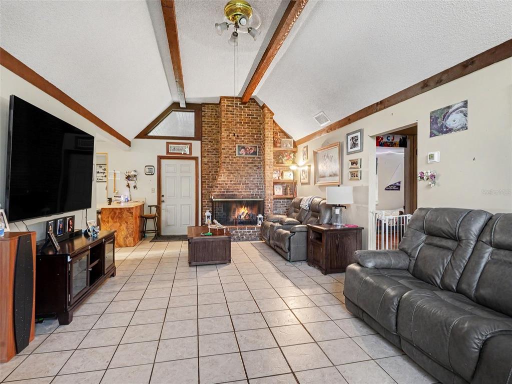 A living room features a vaulted ceiling with wood beams, a brick fireplace, and tile flooring — 128 N POINTE DRIVE, AUBURNDALE, FL