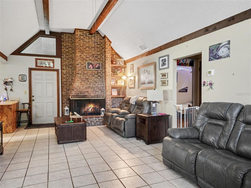 A living room features a brick fireplace, vaulted ceilings with exposed beams, and tiled flooring — 128 N POINTE DRIVE, AUBURNDALE, FL