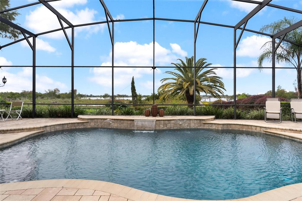 A screened-in swimming pool with a water feature overlooks a lake and palm trees — 1641 EDGEWATER DRIVE, MOUNT DORA, FL