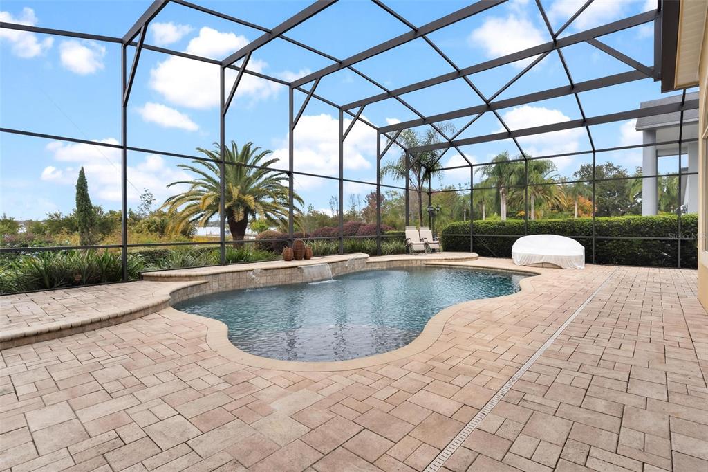 A screened-in pool area features a paver patio, a waterfall, and views of palm trees — 1641 EDGEWATER DRIVE, MOUNT DORA, FL