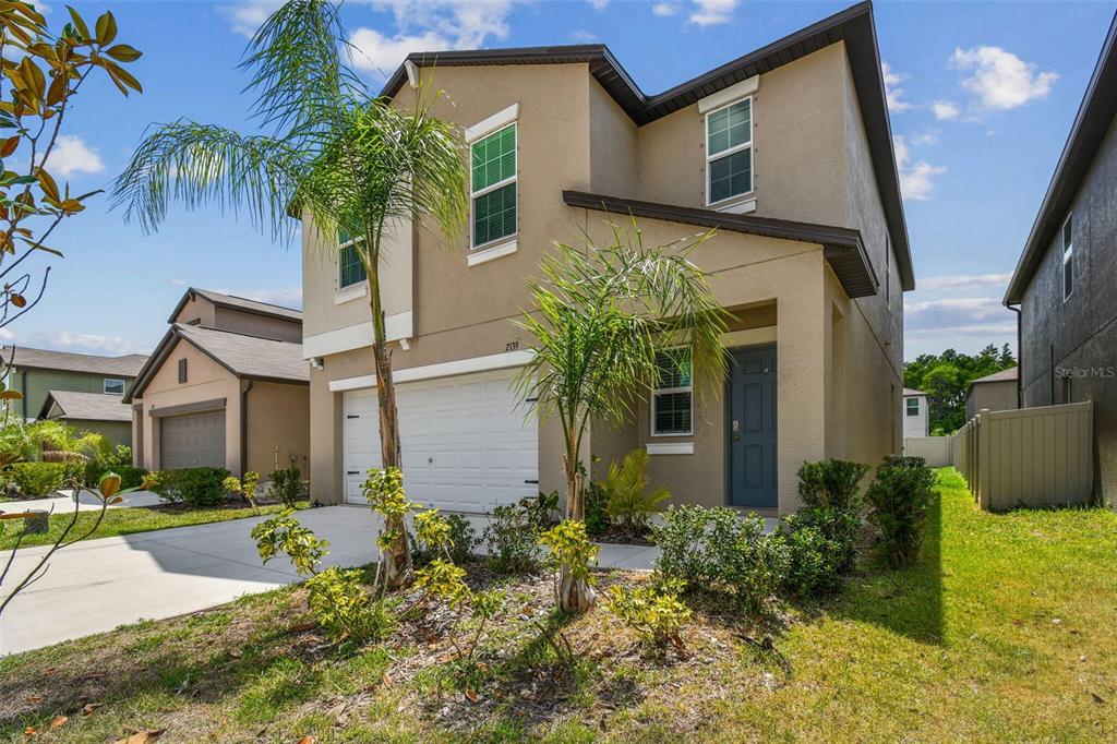 A two-story suburban house with a tan stucco exterior, a two-car garage, and palm trees — 2139 STELLAR BRILLIANCE WAY, LUTZ, FL