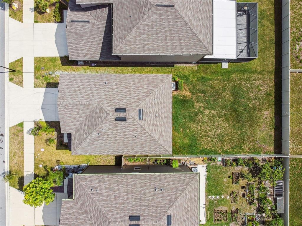 An aerial view shows three suburban houses with shingled roofs and adjacent grassy backyards — 2139 STELLAR BRILLIANCE WAY, LUTZ, FL