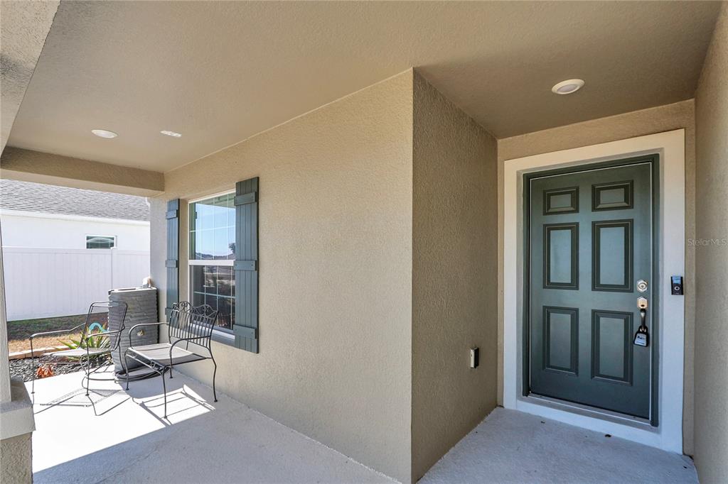 A covered front porch features a dark green door, a window with shutters, and metal furniture — 8968 SE 46TH TERRACE, OCALA, FL