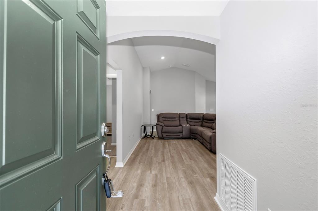 A view from an open green door into a living room with wood-look flooring — 8968 SE 46TH TERRACE, OCALA, FL
