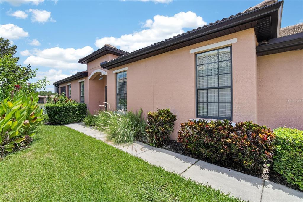 A peach-colored house exterior features a concrete walkway, dark roof trim, and landscaped bushes — 132 SHELL FALLS DRIVE, APOLLO BEACH, FL