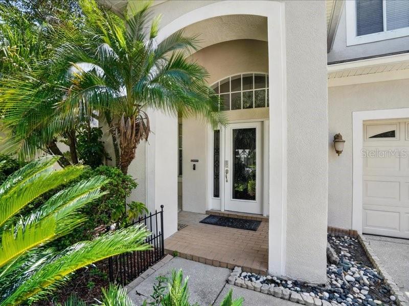 A palm tree stands beside the arched entryway of a house with a white door — 10420 LUCAYA DRIVE, TAMPA, FL