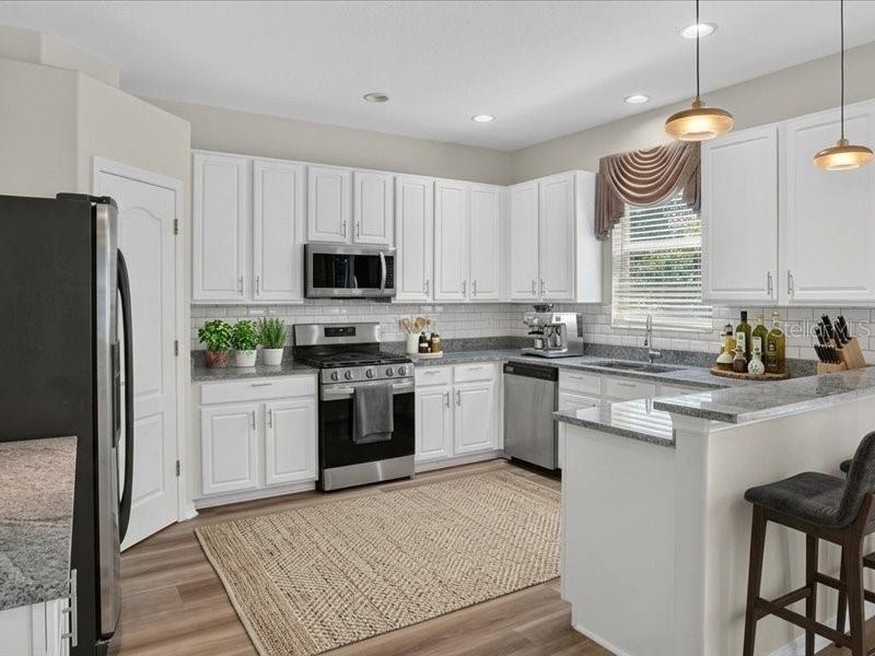 A kitchen with white cabinets, stainless steel appliances, granite countertops, and a light wood floor — 10420 LUCAYA DRIVE, TAMPA, FL
