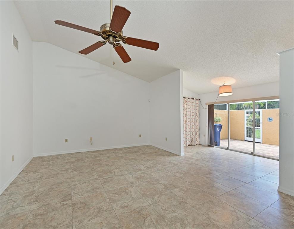An empty living room with vaulted ceilings, a ceiling fan, tile floors, and sliding glass doors — 5506 37TH STREET E UNIT 4, BRADENTON, FL