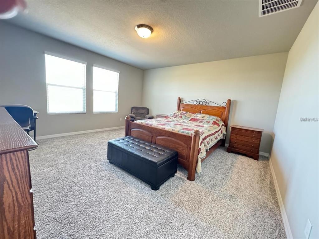 A bedroom features a wooden bed, a black ottoman, and carpeted flooring — 520 WHISTLING DUCK TRAIL, ST CLOUD, FL
