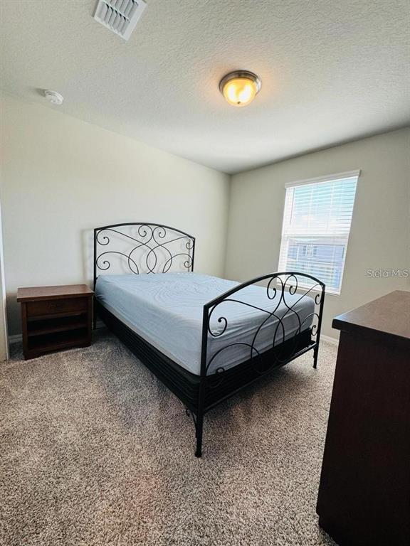 A bedroom features a black metal bed frame, a wooden nightstand, and beige carpeting — 520 WHISTLING DUCK TRAIL, ST CLOUD, FL