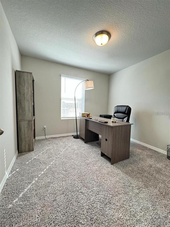 A home office features a desk, chair, bookshelf, and floor lamp on carpeted flooring — 520 WHISTLING DUCK TRAIL, ST CLOUD, FL
