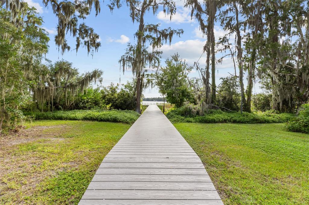 A wooden boardwalk leads through a grassy yard toward a lake surrounded by mossy trees — 6140 SHINER STREET, LAND O LAKES, FL