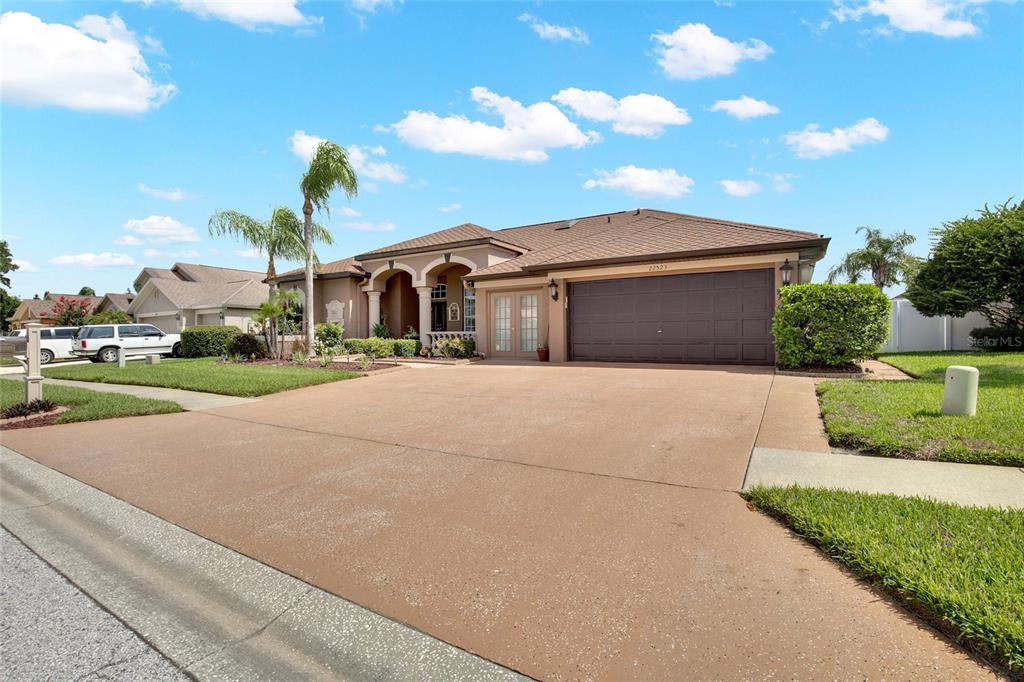 A single-story house with a brown roof, tan stucco exterior, and a large concrete driveway — 22523 WILLOW LAKES DRIVE, LUTZ, FL