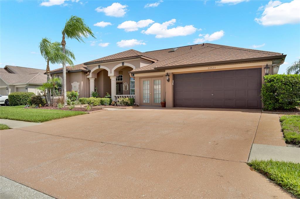 A single-story house with a brown roof, tan stucco exterior, and a two-car garage — 22523 WILLOW LAKES DRIVE, LUTZ, FL