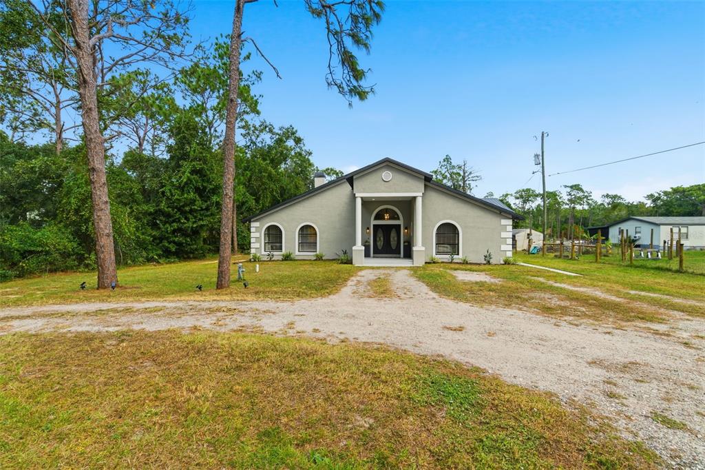A single-story house with a stucco exterior and arched windows sits on a dirt driveway — 28809 BENNINGTON DRIVE, WESLEY CHAPEL, FL