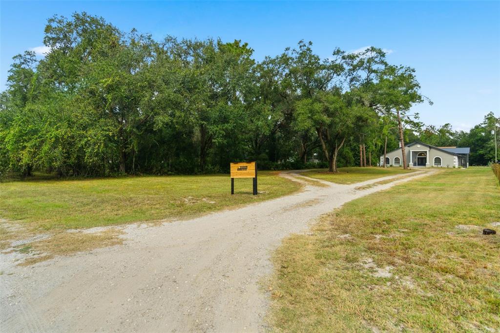 A gravel driveway leads to a house set back behind a large, tree-filled lawn — 28809 BENNINGTON DRIVE, WESLEY CHAPEL, FL