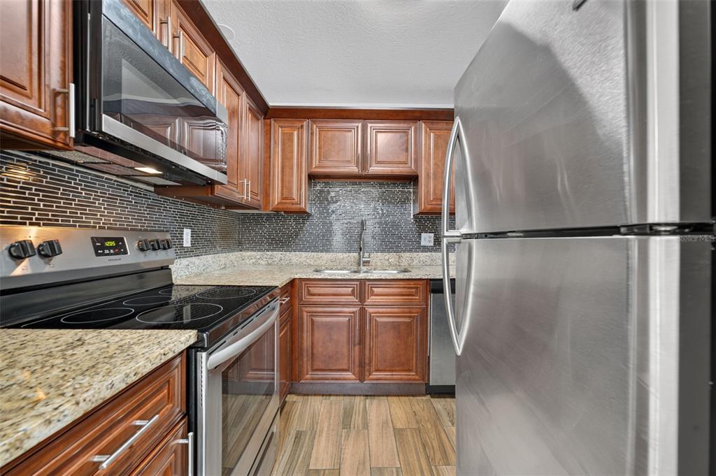A kitchen features dark wood cabinets, granite countertops, stainless steel appliances, and a tiled backsplash — 118 W AMERICA STREET UNIT 2, ORLANDO, FL