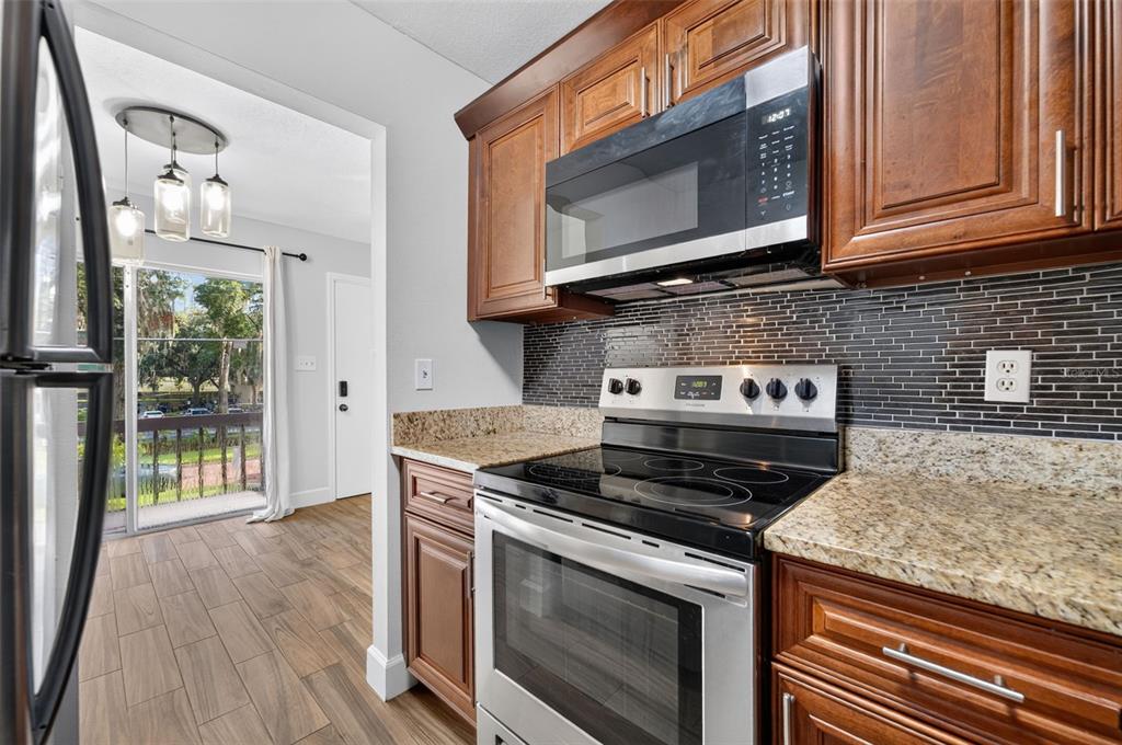 A kitchen with wood cabinets, granite countertops, stainless steel appliances, and a tiled backsplash — 118 W AMERICA STREET UNIT 2, ORLANDO, FL