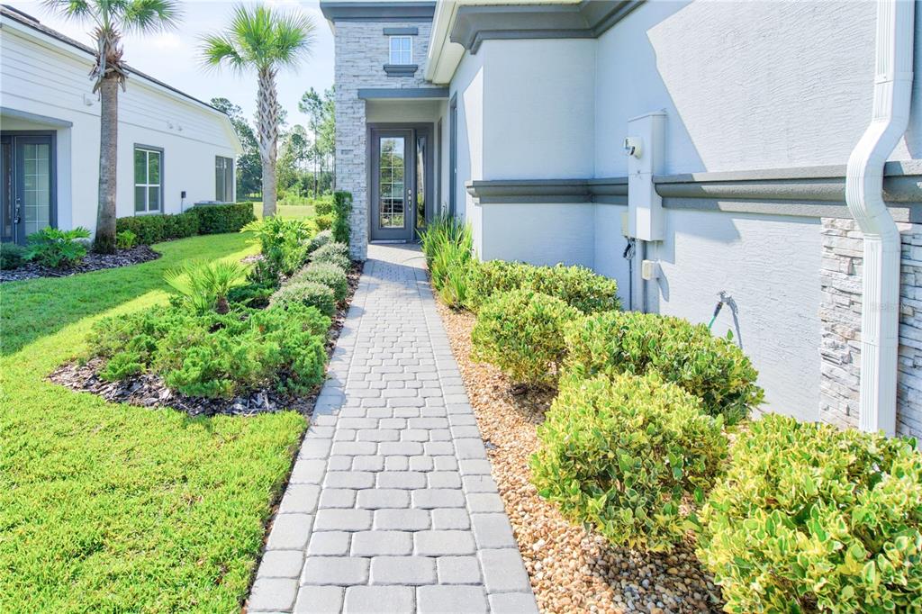 A paved walkway leads to the front entrance of a house with light-colored exterior walls — 30 LONGRIDGE LANE, ORMOND BEACH, FL
