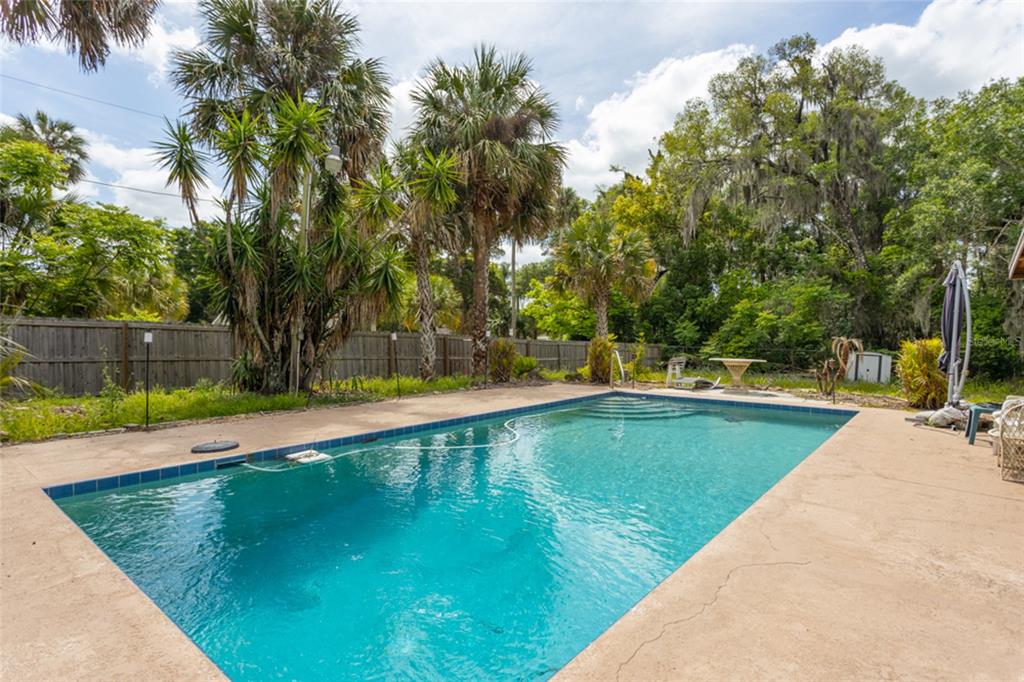 A rectangular swimming pool sits on a concrete patio surrounded by palm trees and fencing — 474 E UNIVERSITY AVENUE, ORANGE CITY, FL