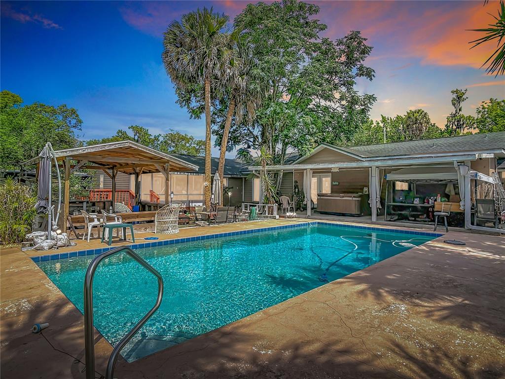 A swimming pool sits on a concrete patio in front of a house with trees — 474 E UNIVERSITY AVENUE, ORANGE CITY, FL