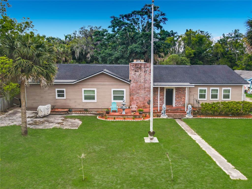 A single-story house with tan siding, a brick chimney, and a large front lawn — 474 E UNIVERSITY AVENUE, ORANGE CITY, FL