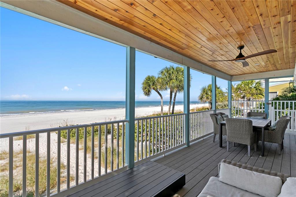 A three-story light blue beach house with balconies stands behind sand dunes and palm trees — 20060 GULF BOULEVARD, INDIAN SHORES, FL