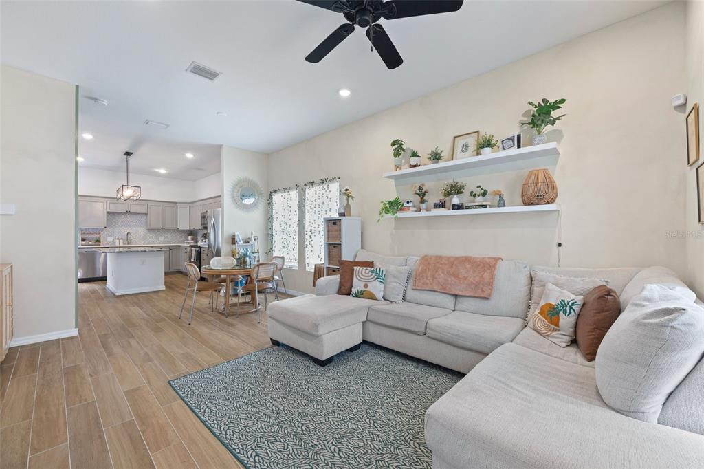 A living room with a sectional sofa and floating shelves opens to a kitchen area — 3403 E 10TH AVENUE, TAMPA, FL