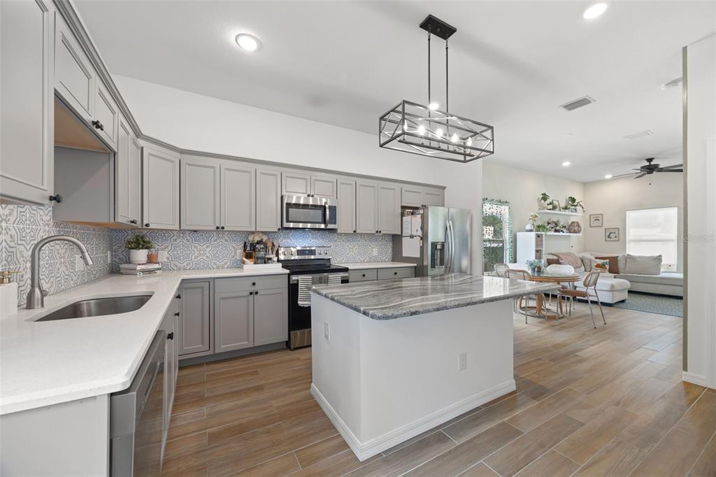 A kitchen with gray cabinets, a stone-topped island, and a patterned tile backsplash — 3403 E 10TH AVENUE, TAMPA, FL