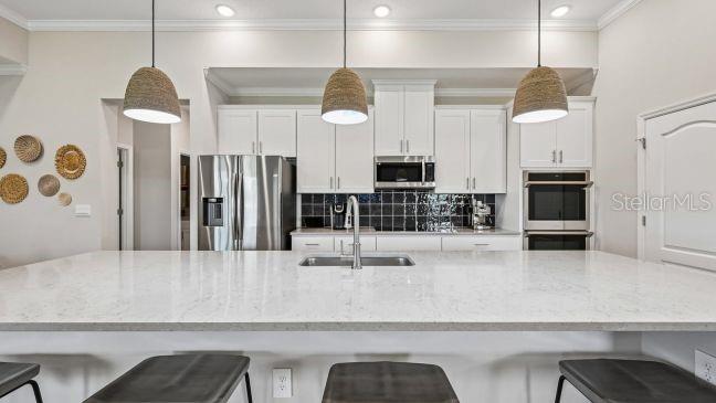 A kitchen features a large quartz island, white cabinetry, stainless steel appliances, and three pendant lights — TBD RAINBOW ROAD, VENICE, FL