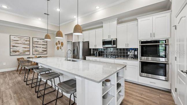 A modern kitchen features white cabinetry, a large quartz island with stools, and stainless appliances — TBD RAINBOW ROAD, VENICE, FL