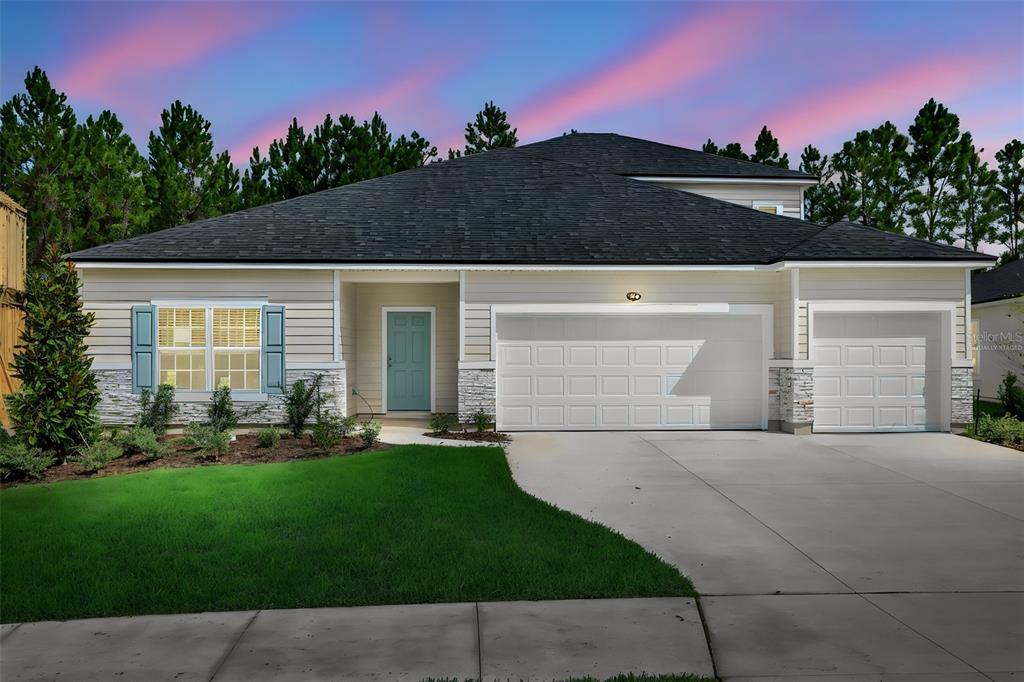 A single-story house with beige siding, stone accents, a three-car garage, and a teal front door — 3702 HOLSTEIN WAY, GREEN COVE SPRINGS, FL