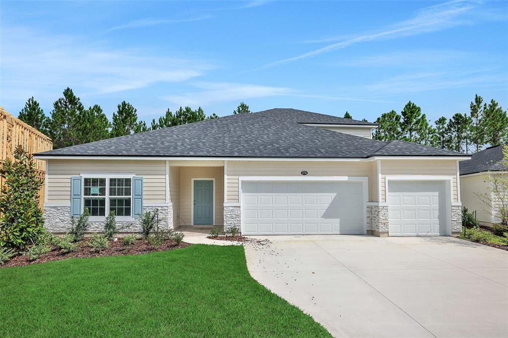 A single-story house with beige siding, stone accents, a two-car garage, and a blue door — 3702 HOLSTEIN WAY, GREEN COVE SPRINGS, FL