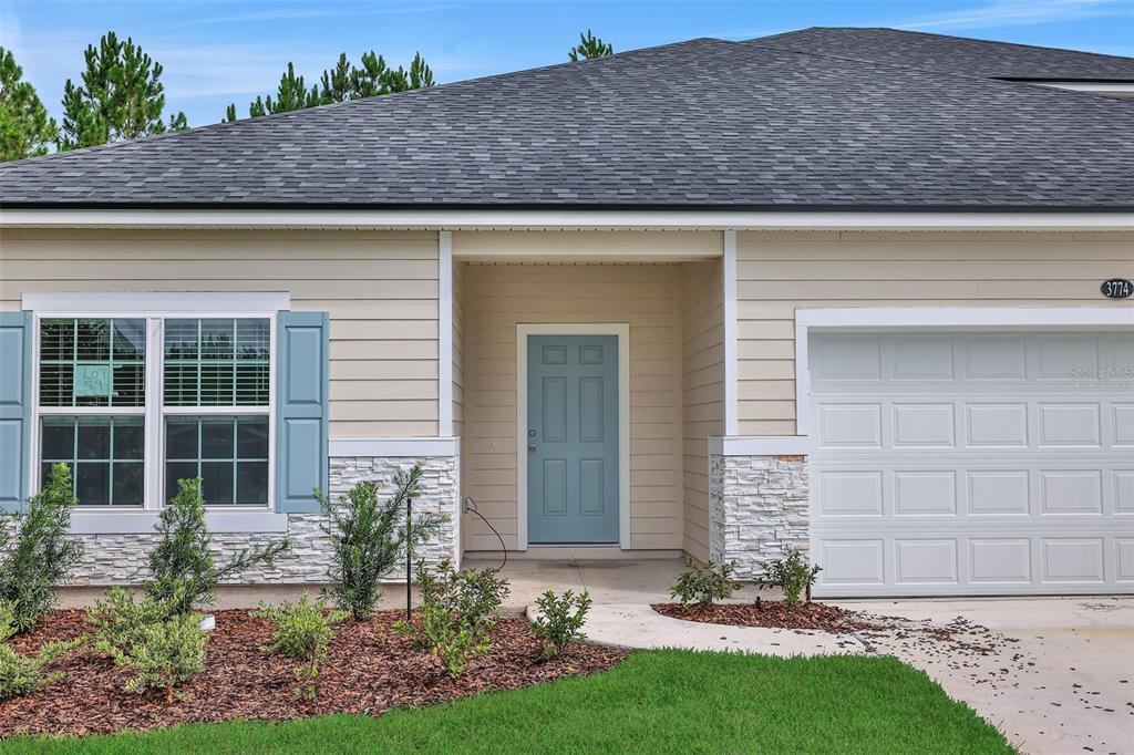 A single-story house exterior features beige siding, a blue front door, and a stone facade — 3702 HOLSTEIN WAY, GREEN COVE SPRINGS, FL