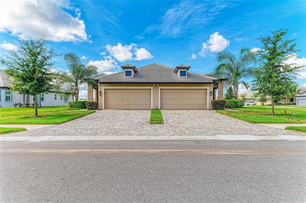 A duplex house exterior features two tan garage doors, a tiled roof, and paver driveways — 17831 CHERISHED LOOP, LAKEWOOD RANCH, FL