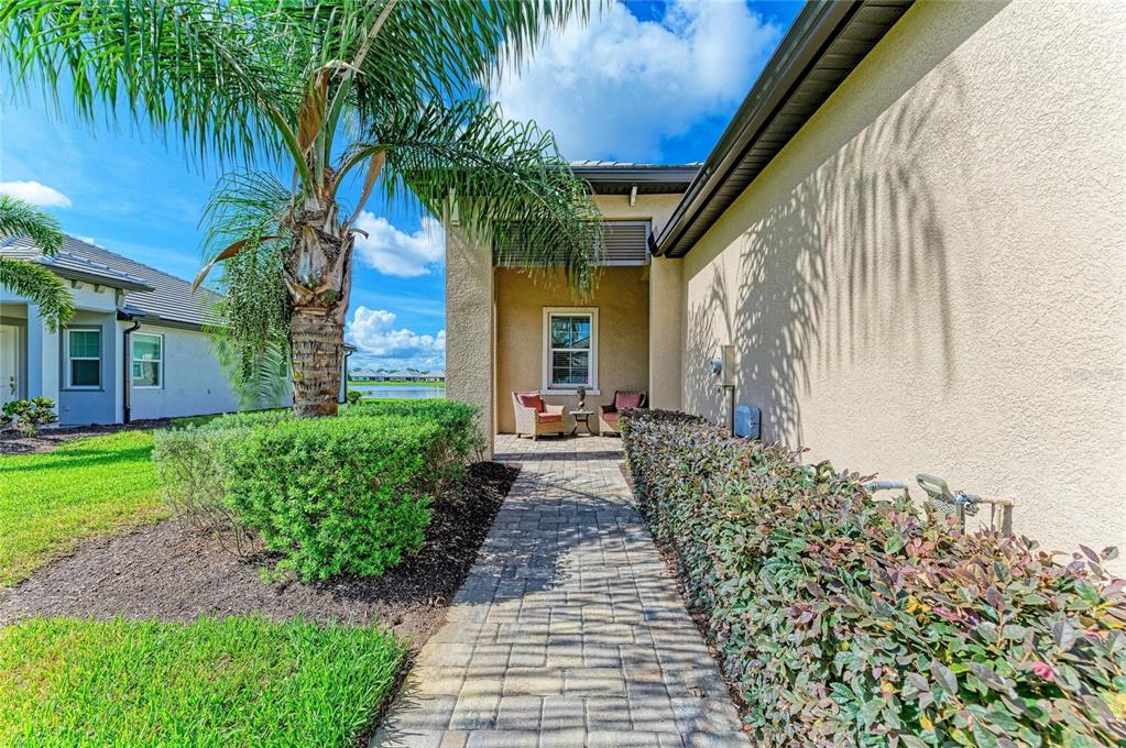 A paved walkway leads to a covered entryway with two chairs beside a house exterior — 17831 CHERISHED LOOP, LAKEWOOD RANCH, FL