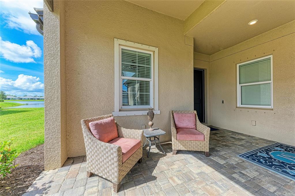 A covered patio features two wicker chairs with pink cushions and a small side table — 17831 CHERISHED LOOP, LAKEWOOD RANCH, FL