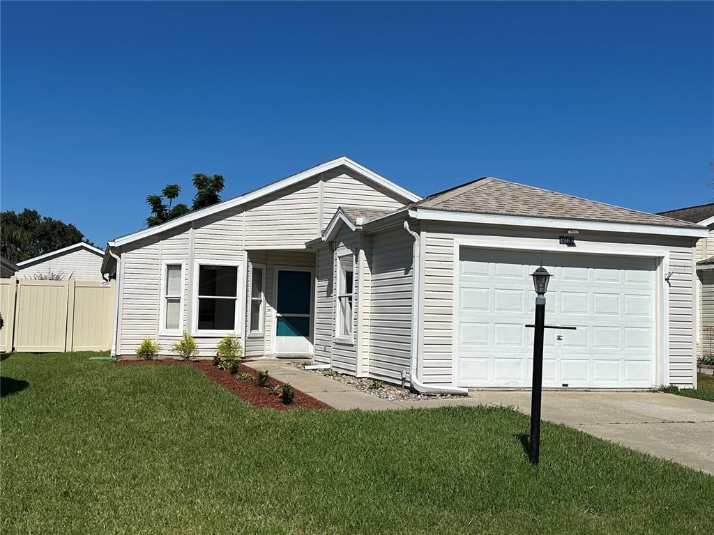 A concrete walkway leads to the front entrance of a house with light-colored siding — 4967 HERON RUN CIRCLE, LEESBURG, FL