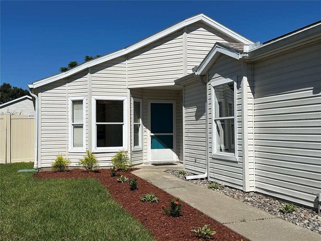 A teal front door with a wreath sits on a porch with light-colored siding — 4967 HERON RUN CIRCLE, LEESBURG, FL