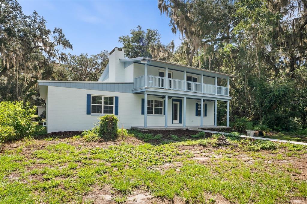 A two-story white house with blue trim and a second-story balcony sits among trees — 177 E COWPEN LAKE ROAD, HAWTHORNE, FL