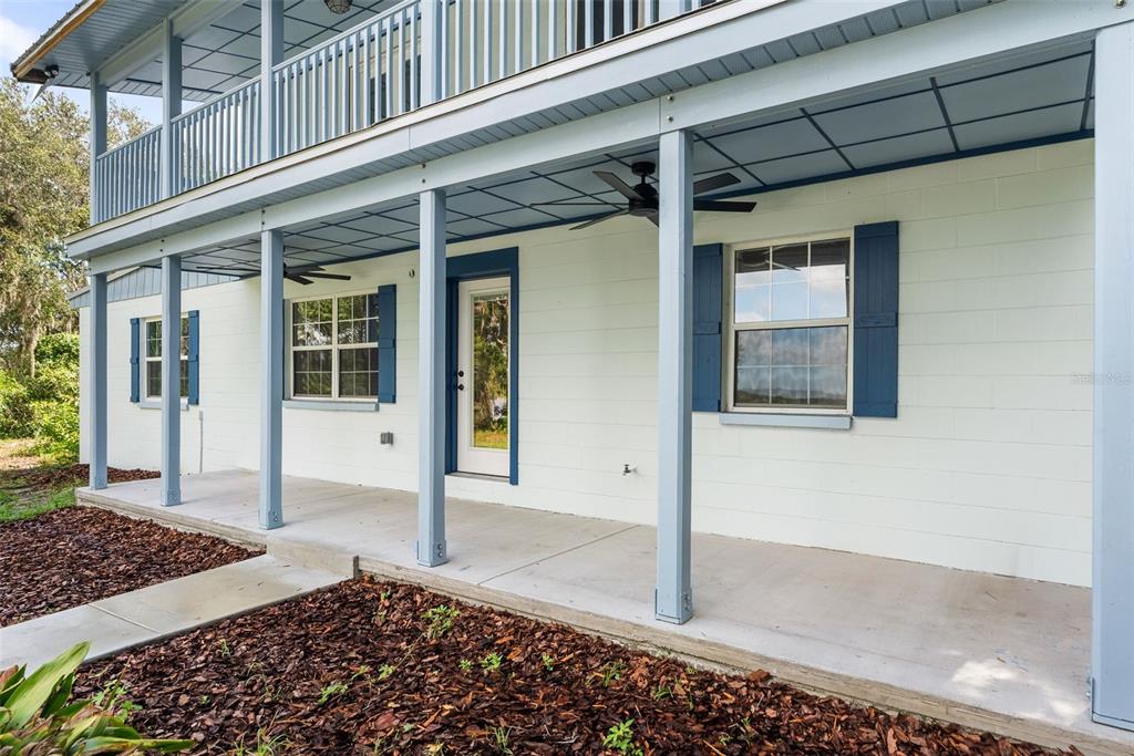 A white concrete block house features a covered porch with blue trim and ceiling fans — 177 E COWPEN LAKE ROAD, HAWTHORNE, FL