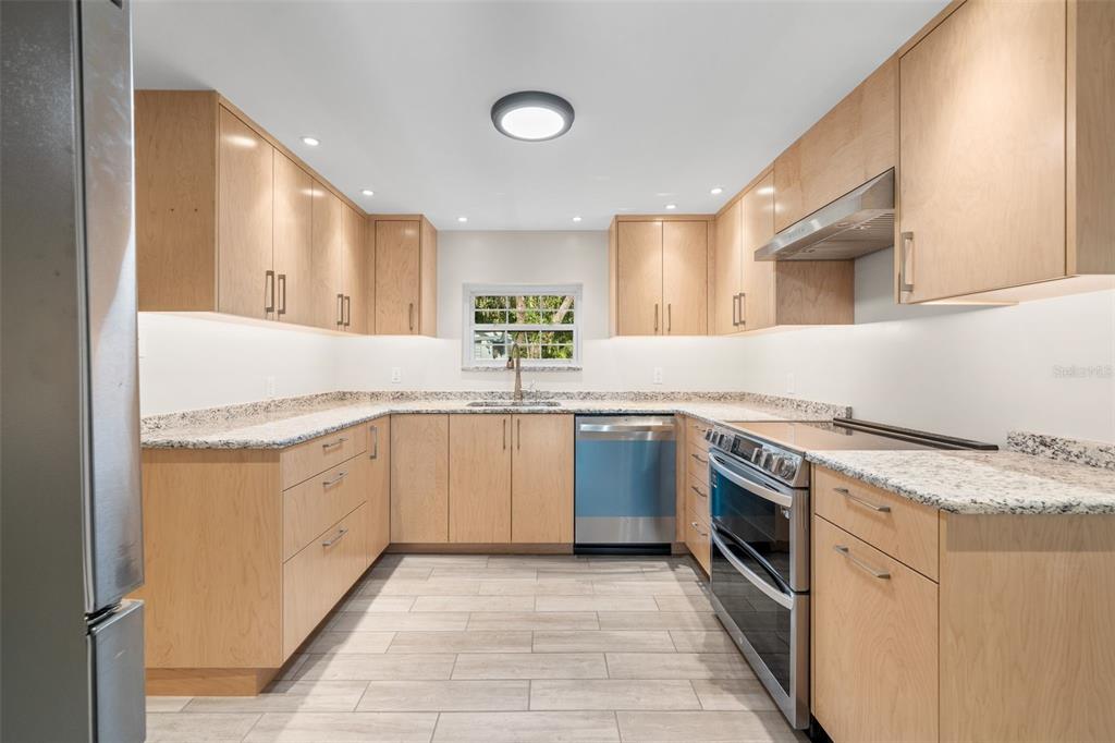 A modern U-shaped kitchen features light wood cabinets, granite countertops, and stainless steel appliances — 177 E COWPEN LAKE ROAD, HAWTHORNE, FL