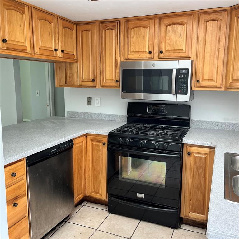 A kitchen features oak cabinets, black appliances, a yellow wall, and gray laminate countertops — 207 BIRCH TERRACE, WINTER SPRINGS, FL