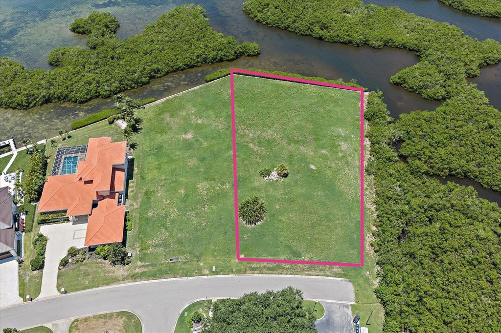 An aerial view shows a vacant, rectangular waterfront lot outlined in pink next to a house — TIDEWOOD AVENUE, SARASOTA, FL